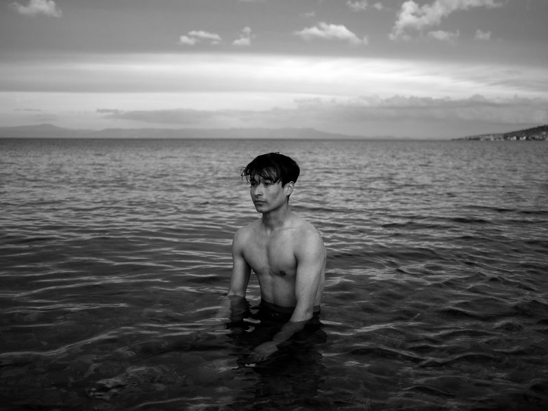 A young man stands inside the sea. Lesvos, Greece, The Island, 2020